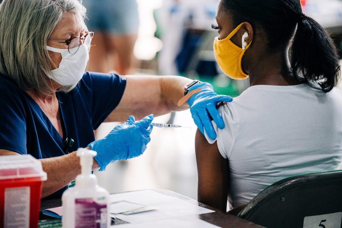 A female health care worker wearing a face mask is vaccinating a black female student wearing a face mask against COVID-19 (Coronavirus Disease) by a health care worker at Bartow Arena, May 18, 2021.