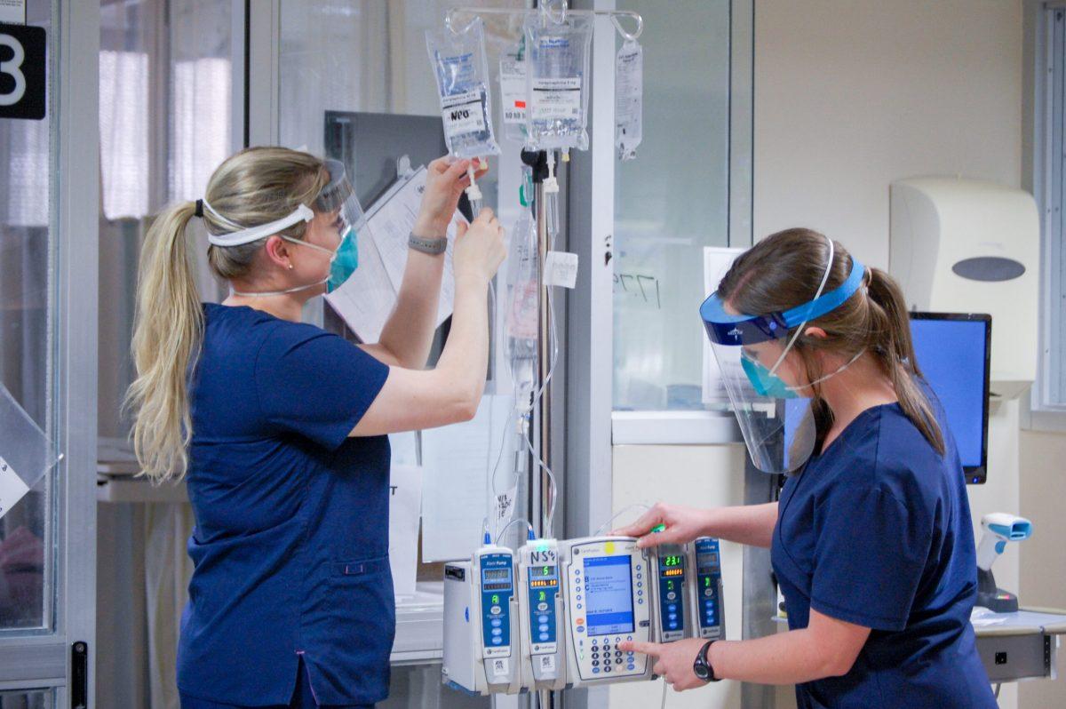 Two unidentified female medical professionals are wearing PPE (Personal Protective Equipment) face masks and shields while working in UAB Hospital during COVID-19 (Coronavirus Disease) pandemic, April 2020.