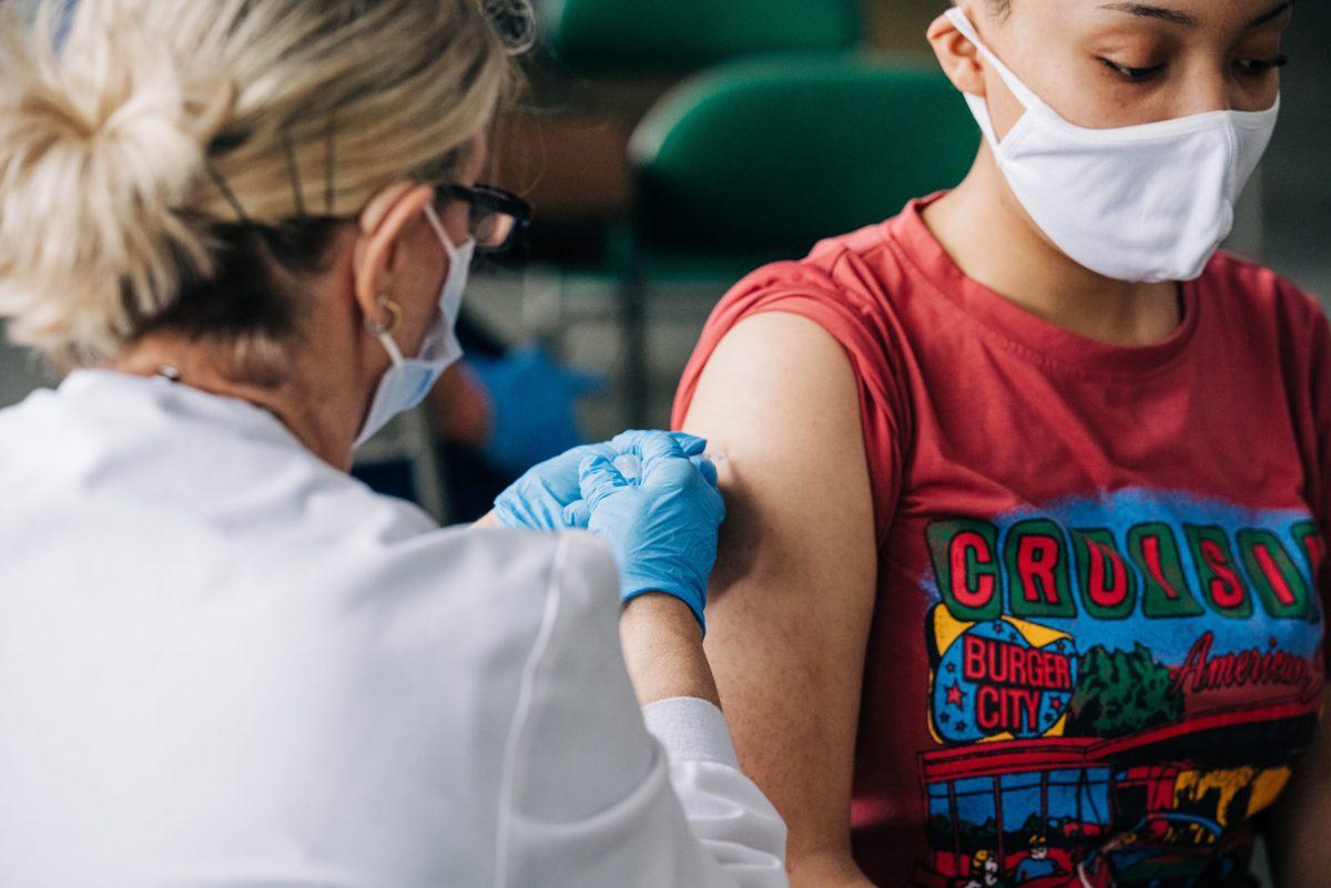 Black female student is wearing a face mask while getting vaccinated against COVID-19 (Coronavirus Disease) by a health care worker also wearing a face mask at Bartow Arena, May 18, 2021.